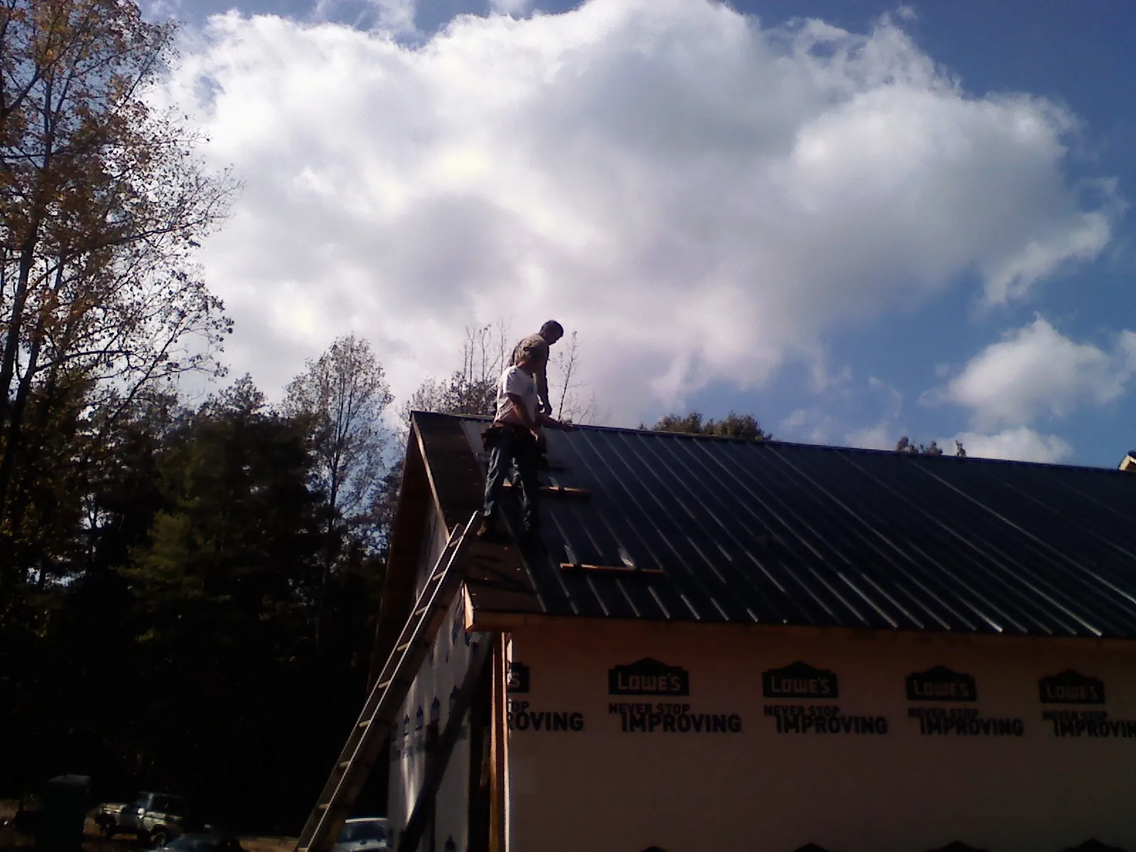 Roofer fastening dark metal panels high against a cloudy sky in Hampton